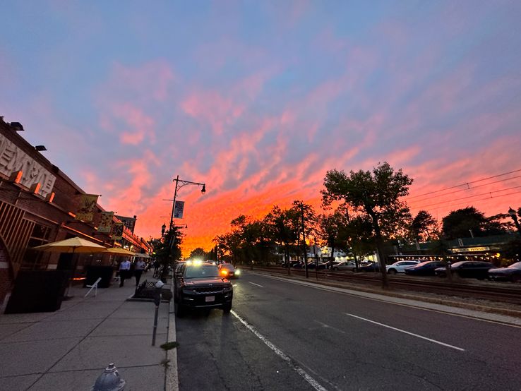 The sun sets beyond Beacon St. - Washington Sq, Brookline. The sky is a bright orange where it meets the horizon